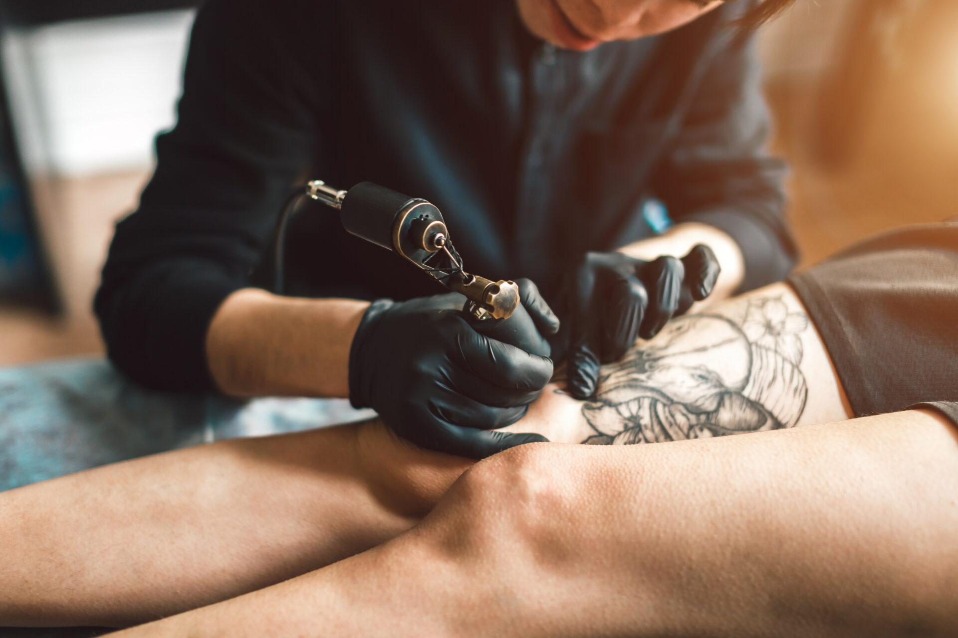 Tattoo artist in black gloves making a tattoo on the leg.